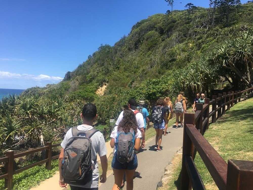 grupo de alumnos de excursión por un camino en la montaña con cielo despejado y mar a la izquierda